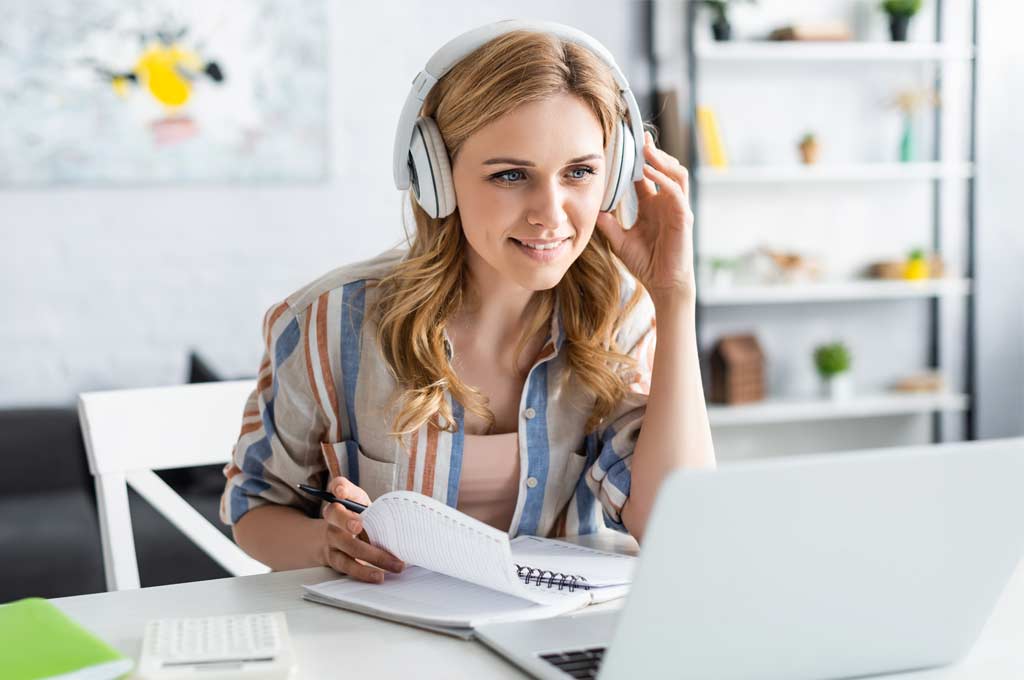 Woman with headphones infront of a laptop learning a language with different devices and different tools - blended learning