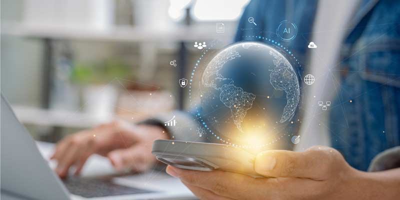 One hand holding smartphone other hand using laptop. The globe hovers over the smartphone screen - digital tools.