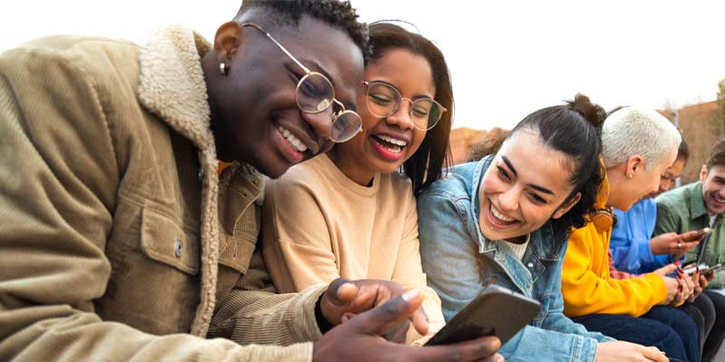 Group a young adults checking a smartphone while laughing - digital natives - the next generation