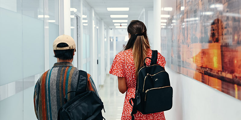 Two learners walking throuhg the hallway, both carrying a backbag