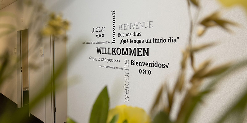 Entrance at inlingua Ostschweiz. White wall written "Willkommen" in different languages.