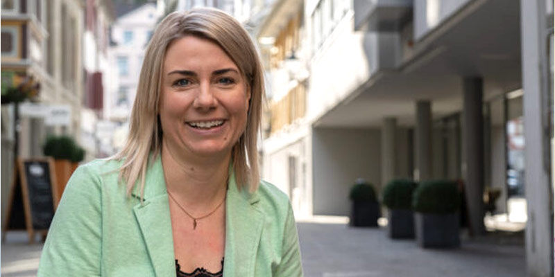 Portrait Picture of Sabrina Bösch, owner of inlingua Ostschweiz. She's wearing a sage green jacket and a black shirt. She has blond hair and is smiling.
