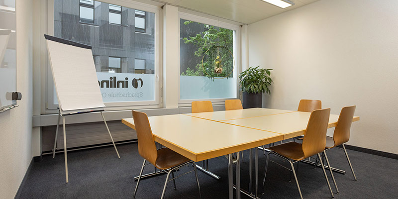empty classroom at inlingua Ostschweiz with a table, chairs, a flower and a flipp chart