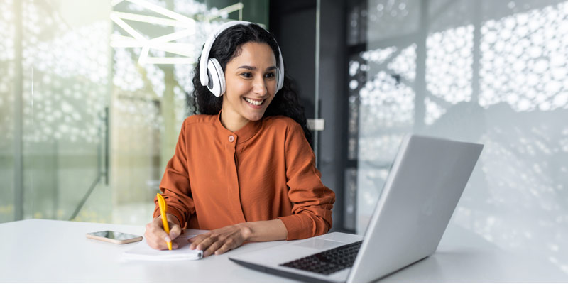 Learner smiling and taking notes during an online lesson on a laptop