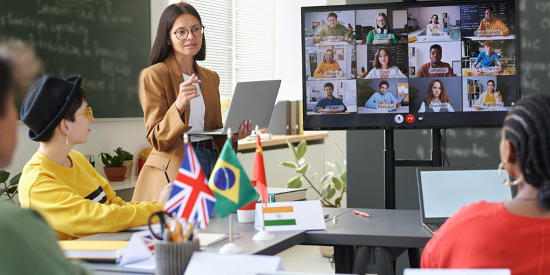 Language trainer teaching a hybrid class with international learners in the classroom and others joining online on a screen