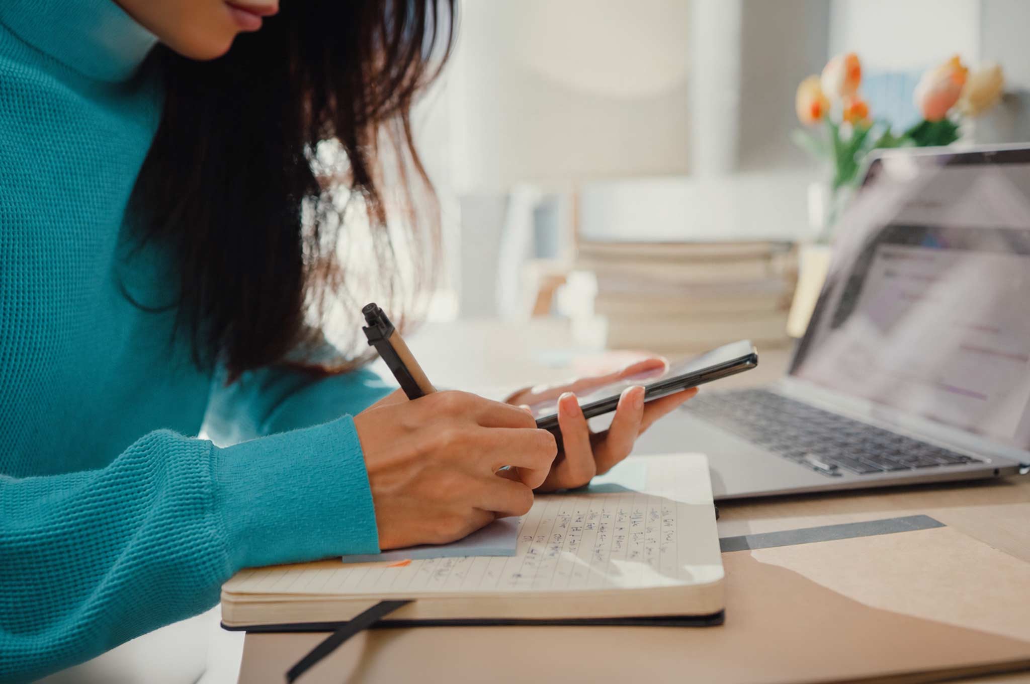 Woman studying a foreign language with a smartphone app and laptop while taking notes at home