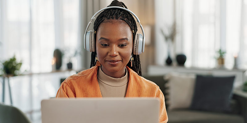 Learner learning a foreign language online with headphones and a laptop in a comfortable home setting