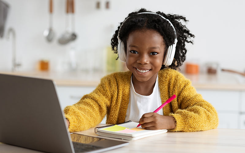 Child learning a foreign language online using a laptop and headphones while taking notes