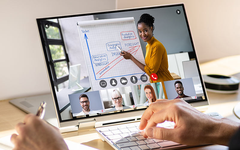 Learner attending a live online lesson on a laptop, with a trainer presenting and other participants visible on screen